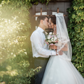 Нежный поцелуй молодоженов возле зеленого плюща в мягком солнечном свете. Свадебный фотограф в Днепре – живые эмоции, природные кадры и красивые детали букета., фото - фотограф Дмтрий Покидин