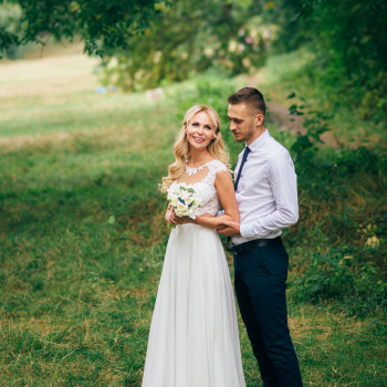 Молодожены на зеленой лужайке под кроной деревьев: невеста с букетом и искренняя улыбка, жених рядом в легком образе, естественные кадры прогулки, мягкий свет и живая атмосфера., фото - фотограф Дмтрий Покидин
