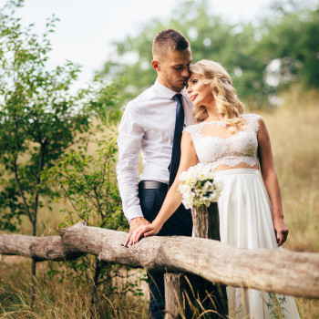 Романтический кадр молодоженов возле деревянного забора на природе: нежный взгляд, легкие прикосновения и букет как акцент. Свадебный фотограф в Днепре — стильные love story, естественный свет и живая атмосфера без лишнего позирования, фото - фотограф Дмт