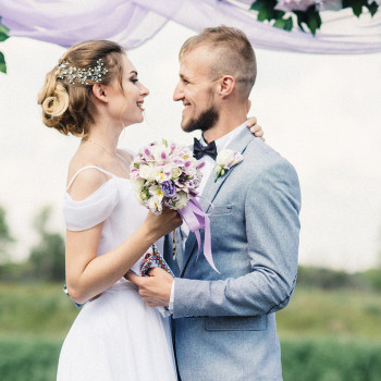 Нежный портрет молодоженов под цветочной аркой: улыбки, взгляды и букет с лиловыми акцентами в центре кадра, фото - фотограф Дмтрий Покидин