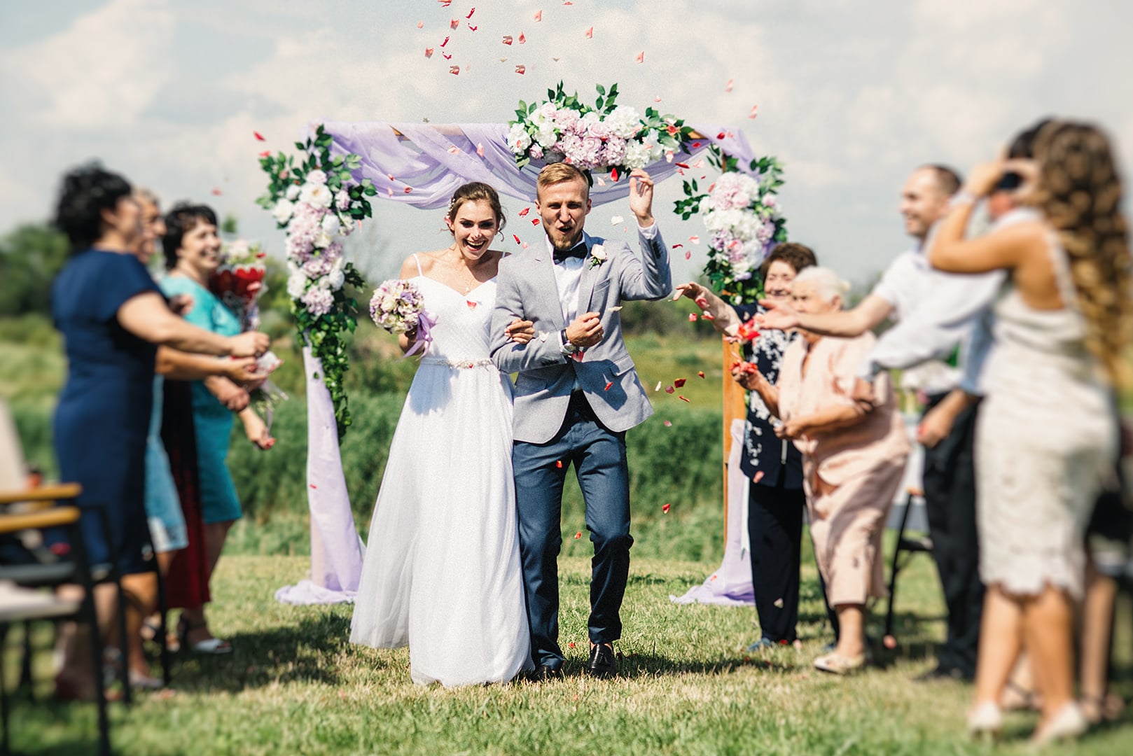 Вибух справжніх емоцій на виїзній церемонії! 🎉 Щасливі молодята проходять крізь "коридор" з гостей, які обсипають їх пелюстками троянд. Цей живий, динамічний репортажний кадр чудово передає атмосферу загальної радості, щирих посмішок та незабутніх моментів свята на природі. Ідеально спіймана мить щастя!, фото - Фотограф Дмитро Покідін