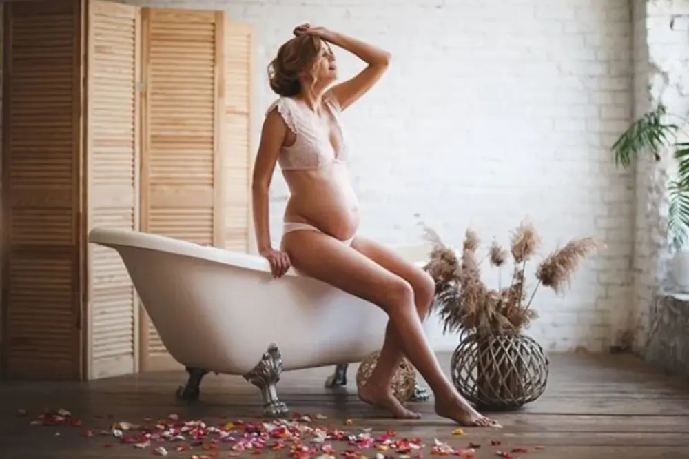 Естетична фотосесія вагітності у світлій студії, де жінка у білизні сидить на краю вінтажної ванни