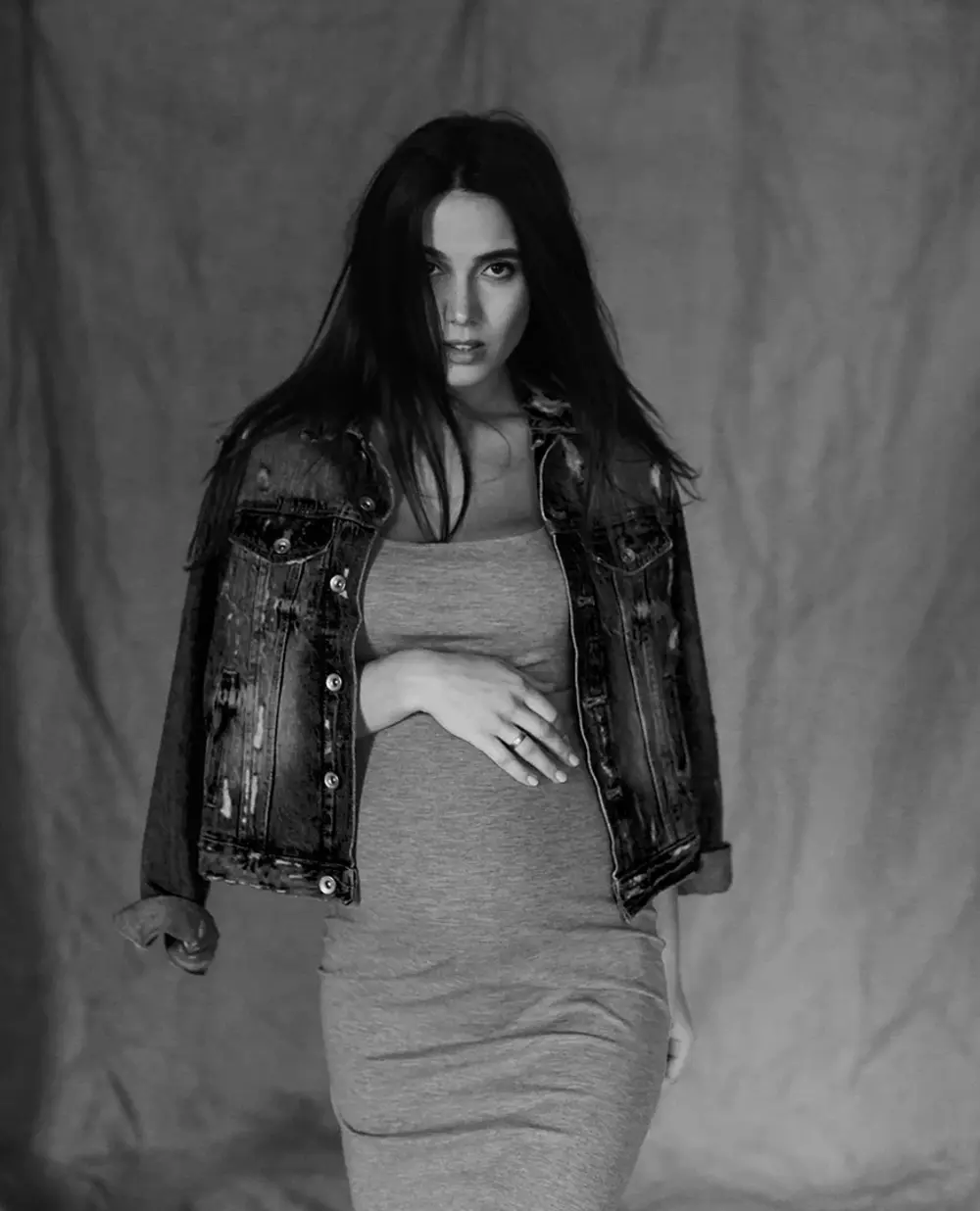 Стильна чорно-біла фотосесія вагітності, де дівчина у джинсовій куртці та сукні тримає руки на животі